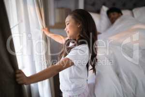 Side view of happy girl holding curtains in bedroom