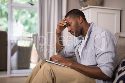 Tensed man using laptop while sitting at home