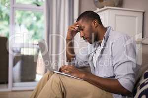Tensed man using laptop while sitting at home
