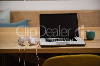 Laptop with headphones and cup on table