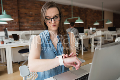 Female executive adjusting smart watch at desk