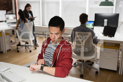 Male executive adjusting a smart watch while colleague discussing in background