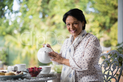 Portrait of smiling mature woman pouring tea in cup