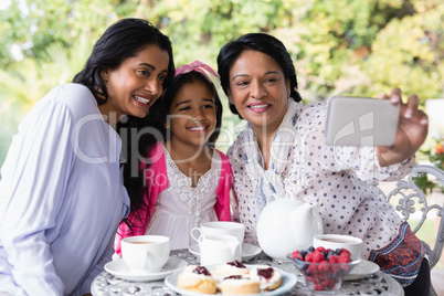 Smiling multi-generation family taking selfie while sitting by breakfast table