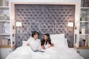 Smiling grandmother and granddaughter talking while sitting on bed