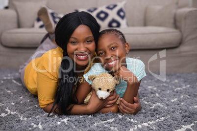 Mother and daughter holding teddy bear while lying on rug at home