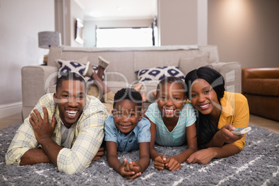 Smiling family watching television while lying on rug at home