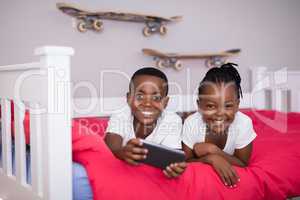 Happy siblings with mobile phone lying on bed at home