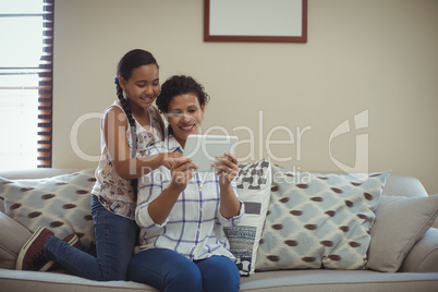 Mother and daughter using digital tablet in living room