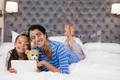 Smiling mother and daughter using digital tablet while lying on bed at home