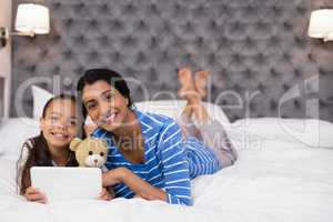 Smiling mother and daughter using digital tablet while lying on bed at home