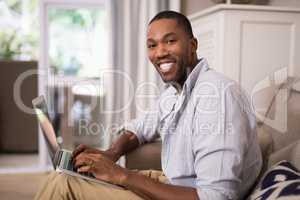 Smiling young man using laptop at home