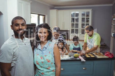 Couple smiling at camera while family members preparing dessert in background