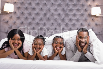 Portrait of smiling family lying together under blanket on bed