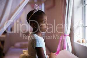Side view of thoughtful girl wearing crown standing in bedroom