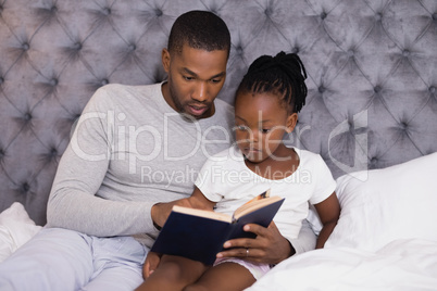 Man with daughter reading book on bed