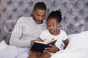 Man with daughter reading book on bed