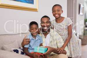 Smiling father and children holding gift box on sofa at home