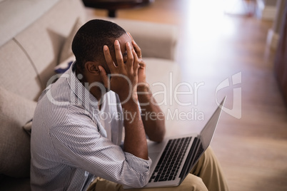 Frustrated man with laptop sitting at home