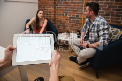 Executive using digital tablet and colleagues discussing in background