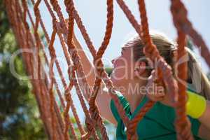 Determined woman climbing a net during obstacle course training