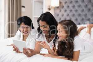 Happy multi-generation family using digital tablet while lying on bed
