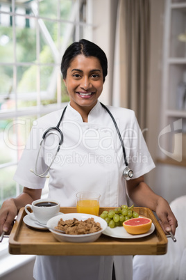 Smiling nurse holding breakfast tray at home