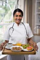 Smiling nurse holding breakfast tray at home