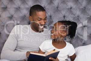 Happy man with daughter reading book on bed
