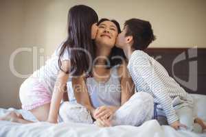 Siblings kissing mother on cheeks in the bed room