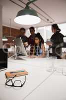 Spectacles with notebook on table while colleague discussing in background