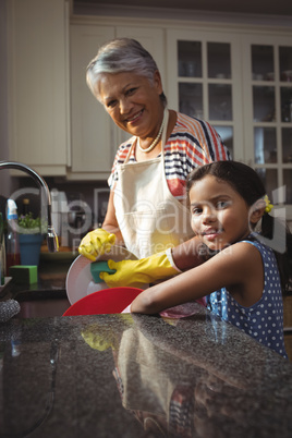 Grandmother and granddaughter washing utensil in kitchen sink