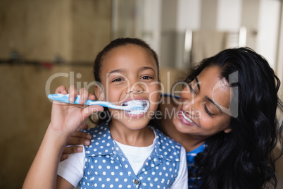 Portrait of girl brushing teeth with mother in bathroom