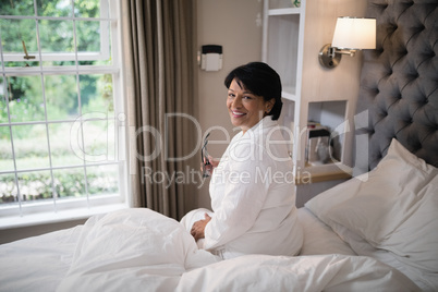 Smiling mature woman sitting in illuminated bedroom at home