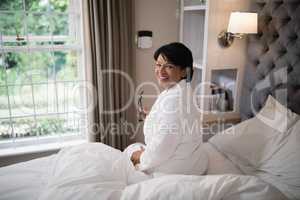 Smiling mature woman sitting in illuminated bedroom at home