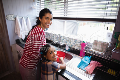 Portrait of smiling girl helping her mother in kitchen