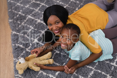 Mother and daughter with teddy bear while lying on rug at home