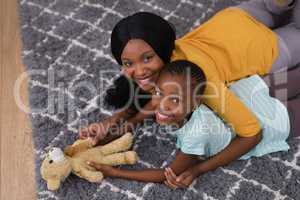 Mother and daughter with teddy bear while lying on rug at home