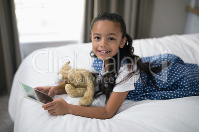 Smiling girl using digital tablet while lying on bed at home