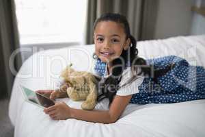Smiling girl using digital tablet while lying on bed at home