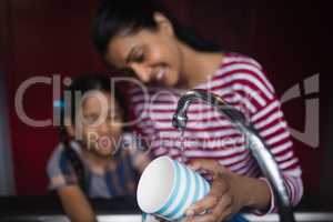 Smiling woman with daughter washing cup at sink
