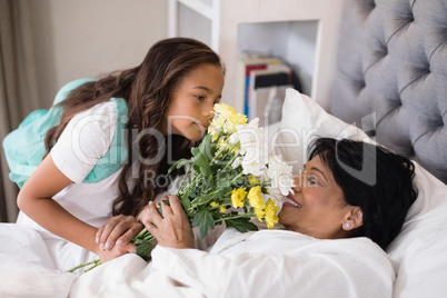 Girl giving bouquet to sick grandmother at home