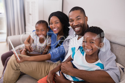 Portrait of cheerful family using digital tablet while sitting on sofa