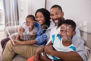 Portrait of cheerful family using digital tablet while sitting on sofa