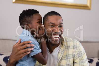 Boy whispering father on sofa at home