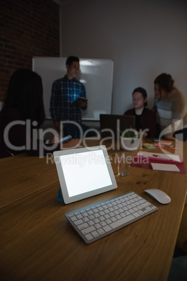 Digital tablet on table while colleague discussing in background