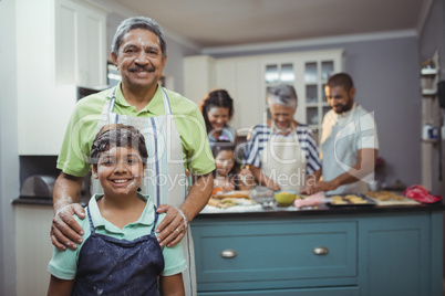 Grandfather and grandson smiling at camera while family members preparing dessert in background