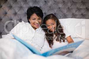 Happy grandmother and granddaughter reading book on bed