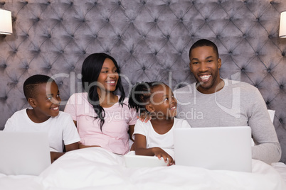 Portrait of smiling man using laptop while sitting with family on bed