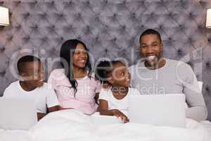 Portrait of smiling man using laptop while sitting with family on bed